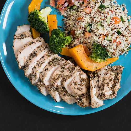 Sliced Italian herb-roasted chicken breast, photographed on a plate with couscous salad, broccoli and pumpkin. Serving suggestion.