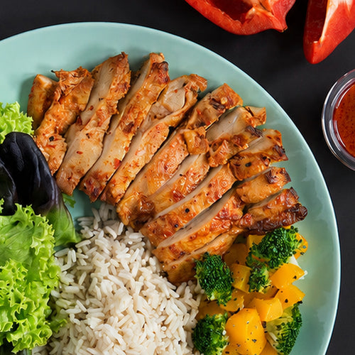 Sliced sambal-spiced chicken breast, photographed on a plate with rice, lettuce and roasted vegetables. Serving suggestion.